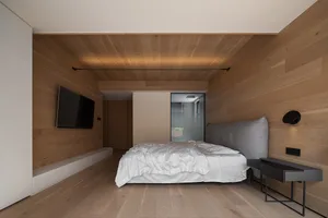 Modern, minimalist bedroom featuring wooden walls, a neatly made bed with white bedding, and a sleek, uncluttered design.