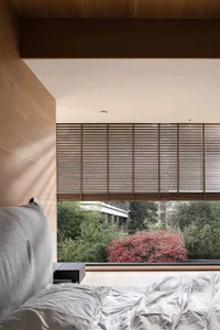 A modern bedroom featuring wooden blinds on the window, with a cozy bed and minimalist decor.