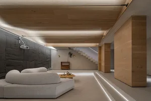 A modern minimalist living room with a white sofa, a round wooden coffee table, and a projector setup on a black, stone-like 