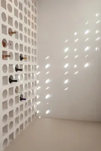 A minimalist concrete wall with wine storage holes casts intricate shadows on the adjacent wall, creating a pattern of light 