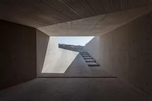 Modern interior space with concrete walls, stairs leading down to a lightwell, and a view of the outdoors.