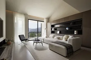 A modern living room featuring white furniture and minimalist decor, with large windows providing natural light and scenic vi