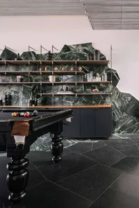 An industrial-style recreation room featuring a black pool table and a wall of shelves against a green marble backdrop.
