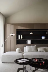 A modern minimalist living room featuring beige upholstered furniture, wooden cabinets, and a black coffee table with red app