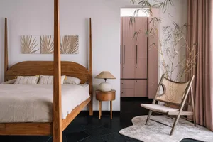 A modern bedroom featuring a wooden four-poster bed, a side table with a lamp, and a chair with a wicker backrest.