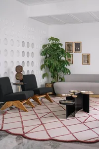 Photograph of a modern living room with a minimalistic design featuring a grey sofa, black chairs, a unique coffee table, and