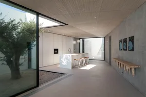 Modern residential interior featuring sleek, minimalist design with concrete flooring, glass walls, and a central kitchen isl