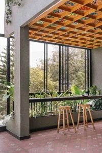 A cafe interior design featuring a wooden ceiling adorned with colorful floral patterns, potted plants, and a table with stoo