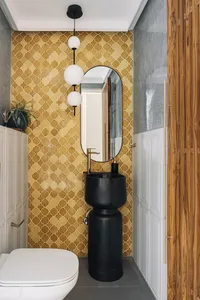 A modern bathroom featuring yellow geometric patterned tiles, a black pedestal sink, and a white toilet.