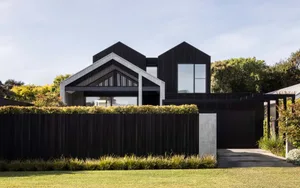Modern black wooden exterior house with a fence and garden hidden behind it.