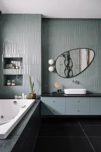 Modern bathroom with green tiles, black floor, and a freestanding tub.