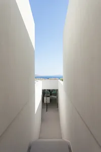A narrow corridor with concrete walls and white flooring leading to a view of the sea.