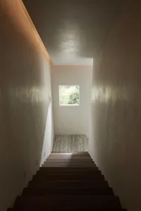 Modern indoor staircase with wooden steps, warm lighting, and a small rectangular window at the top.