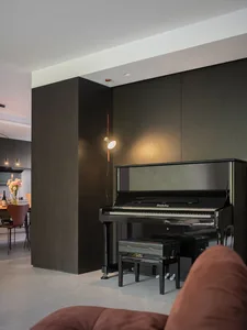 A minimalist living room featuring a piano corner with wooden cabinets and a brown sofa.