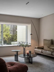 Modern living room with minimalist decor featuring a round table, vase with flowers, and a long modern floor lamp.