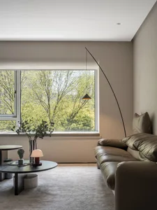 A cozy modern living room with a circular side table, green plants, and a large window overlooking trees.