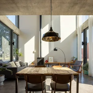 A spacious, modern living and dining area featuring exposed concrete beams, wooden dining table, and contemporary decor.