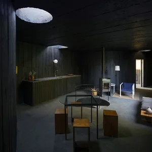 A minimalist kitchen with a concrete floor, walls, and table, and wooden stools.