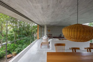 Modern minimalist living room featuring concrete walls and a large outdoor balcony overlooking lush greenery.