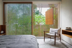 A modern bedroom with glass walls and a single white armchair.