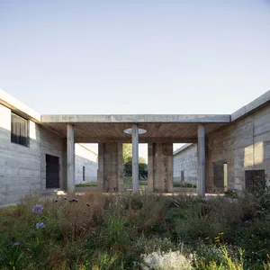 Concrete columns supporting an open space with wildflowers and grass in the foreground, under a clear sky.
