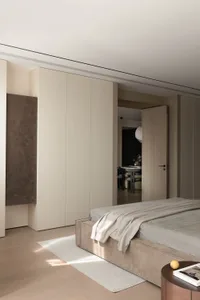 A modern bedroom featuring a bed with a neutral-toned blanket and a large closet in the same color palette.