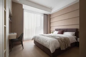 A modern bedroom featuring a bed with a dark headboard, light-colored bedding, and a window with sheer curtains.