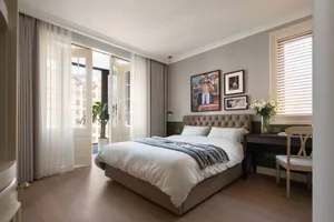 A minimalist bedroom featuring a comfortable bed, elegant furniture, and artistic wall decor, bathed in soft, natural light.