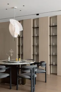 Minimalist dining room with a round marble table, wooden chairs, flat-panel shelving, and floating light fixture.