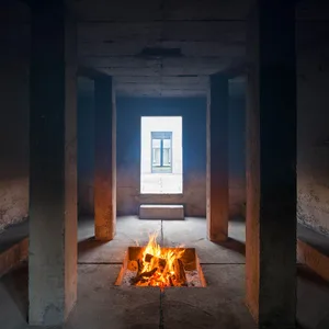 A minimalist interior with concrete walls, a burning fire pit, and a small window in the distance.