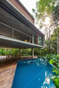 A modern concrete residence featuring a glass patio and a swimming pool surrounded by lush greenery.