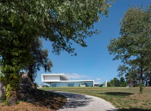 A modern house with glass walls sits on a hillside.