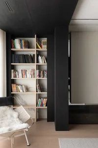 A modern home library featuring wooden shelving filled with books and a cozy armchair on a wooden floor.