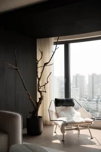 簡約客廳空間，窗邊擺放木質扶手椅與插有樹枝的花瓶。