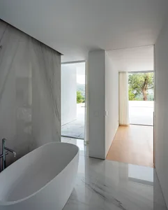 Modern minimalist bathroom with white marble finishes and glass enclosure.