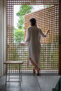 A modern interior space featuring a white rope stool in front of a wooden lattice fence and a woman in a white robe standing