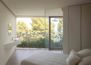 A minimalist bedroom with glass walls and a view of greenery.