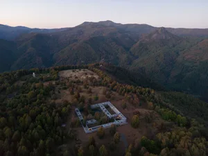 An aerial view of a modern architectural structure surrounded by dense forests and mountains.