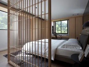 A minimalist bedroom featuring a wooden bed frame and windows overlooking greenery.