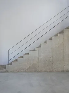 Minimalist, industrial-style staircase with concrete steps and a steel handrail against a white wall.