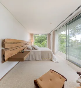 A minimalist bedroom featuring a wooden headboard, a carpeted floor, and a bed with pillows, situated in front of a large win