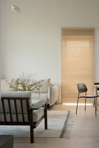 Minimalist living room with wooden flooring, white walls, and a window with wooden blinds, showcasing budget-friendly design