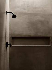 A minimalist concrete bathroom shower with a black showerhead mounted on the wall.