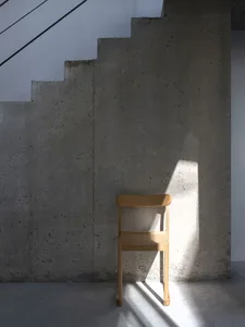 A minimalist staircase with concrete steps and a wooden chair in front of it.