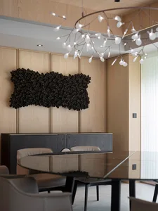 Modern dining room featuring sleek wooden walls, glass table with metal legs, and contemporary light fixture.