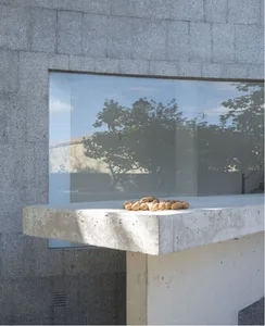 A modern exterior featuring a concrete wall with a large glass window and patio.