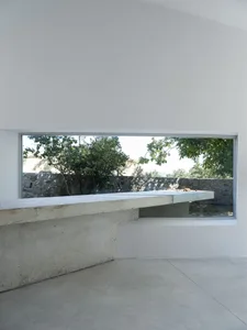 A modern interior featuring minimalist design with concrete walls and floor, large window with outdoor view.