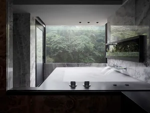 Modern minimalist bathroom with marble fixtures, large window overlooking greenery, and water feature.
