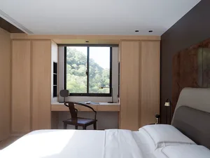 Modern minimalist bedroom with white wood-paneled walls and cabinets, featuring a white bed with pillows, a desk area by the