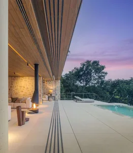 A modern residential exterior featuring a concrete floor, wooden ceiling, and fireplace, with a poolside lounge area and a vi